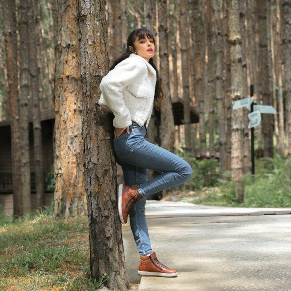 woman leaning towards a tree with brown boots